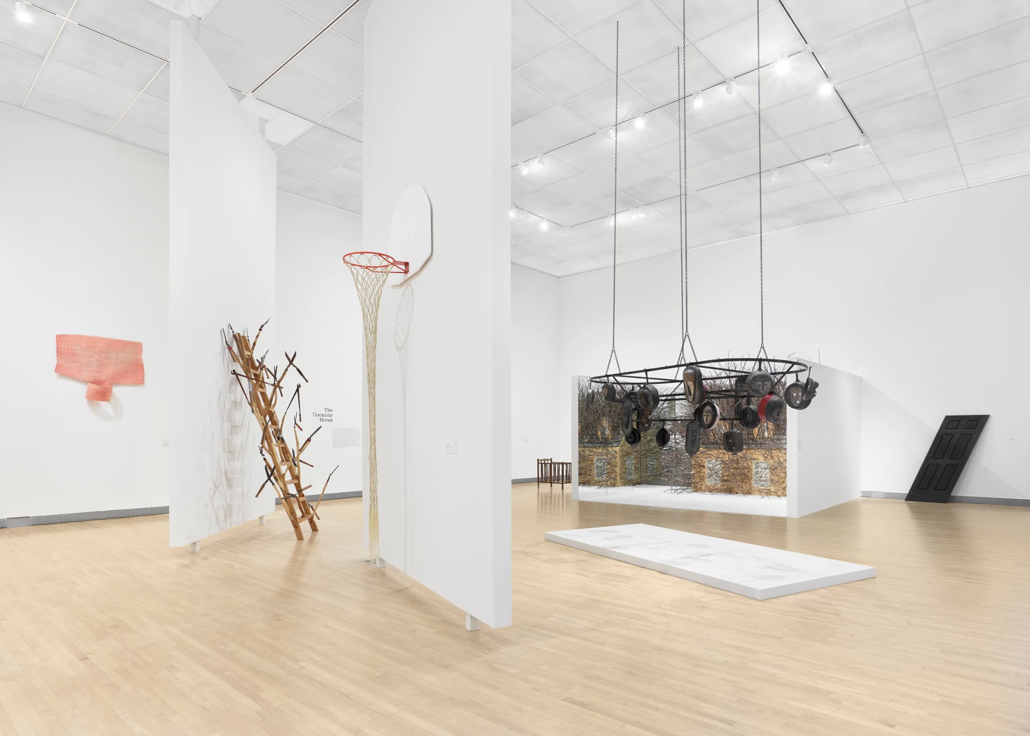 Wooden sculptures and a woven basketball net in a gallery.
